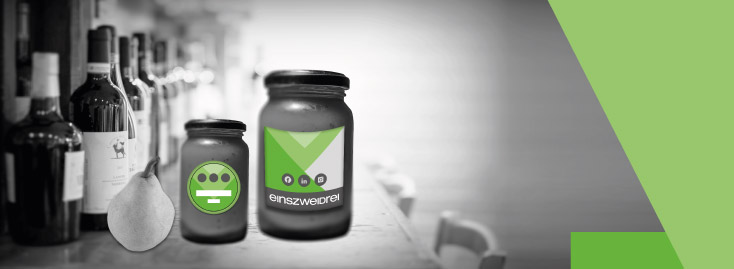 Eine Hand hält eine Karte mit grünen Akzenten und dem Wort „WUNSCHFORMAT“ in fetten Buchstaben vor einer Reihe von Flaschen und Gläsern auf einer Theke; der Hintergrund ist schwarz-weiß, während die Karte und geometrische Formen an der Seite grün gefärbt sind.