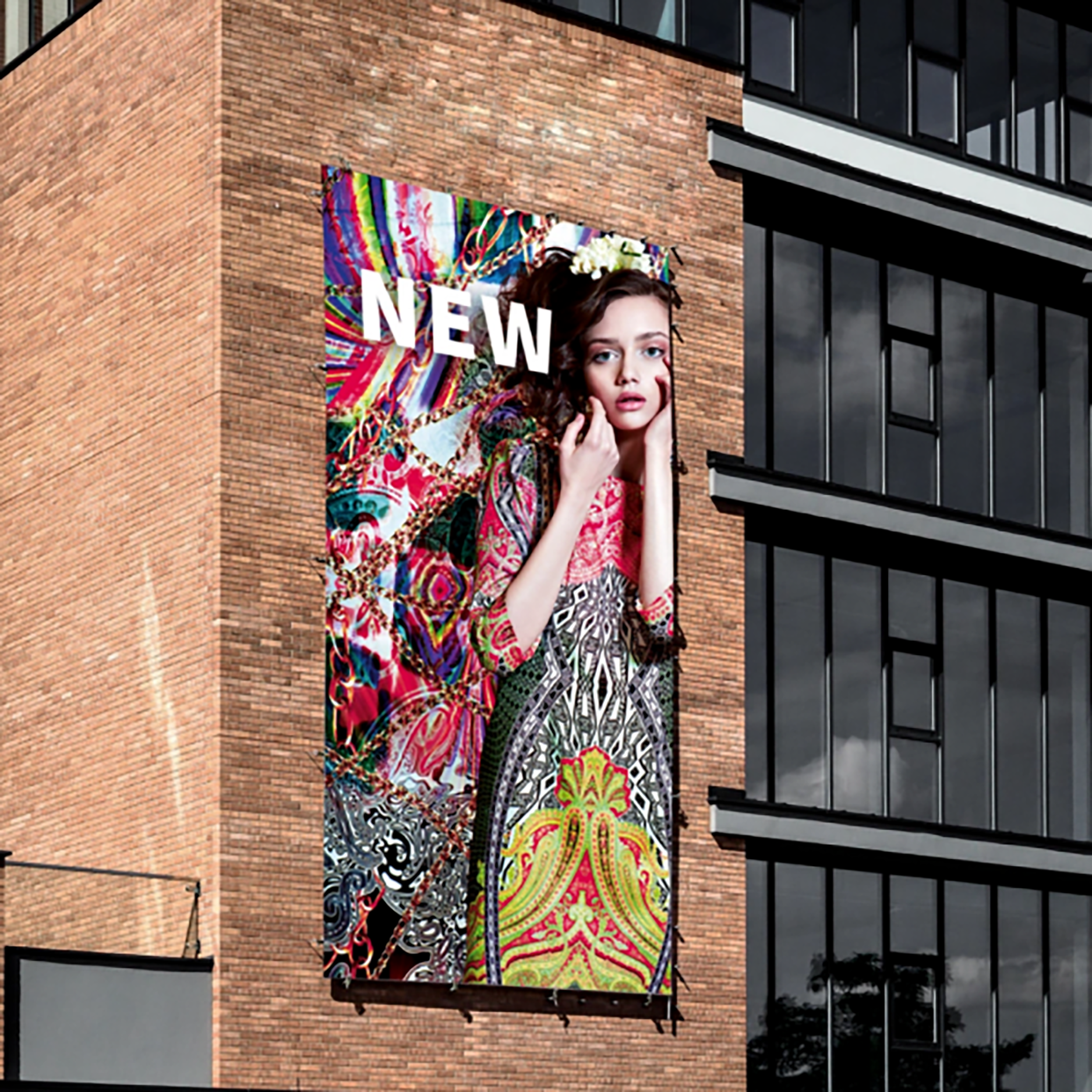 A large, colorful fashion advertisement is displayed on the side of a brick building, featuring a woman in a vibrant patterned dress with the word