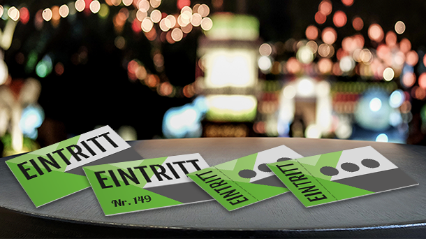 Auf einem runden Tisch liegen vier grün-weiße Eintrittskarten mit der Aufschrift „EINTRITT“. Im Hintergrund deuten bunte, unscharfe Lichter auf eine festliche oder Event-Atmosphäre hin.