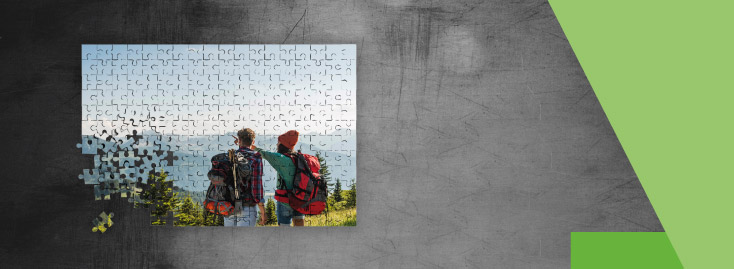 Ein weißes Kissen mit einem aufgedruckten Foto von zwei Personen mit Rucksäcken, die im Freien stehen und eine Berglandschaft betrachten, vor einem grauen Hintergrund mit grünen geometrischen Akzenten.