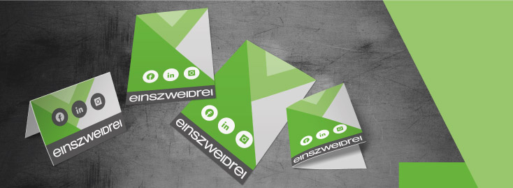 Ein Satz grüner und weißer gefalteter Immobilienflyer mit dem Text „einszweidrei“ und Social-Media-Symbolen für Facebook, LinkedIn und Instagram, dargestellt auf grauem Hintergrund mit einem grünen Akzent auf der rechten Seite.