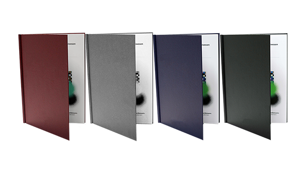 Vier gebundene Dissertationsbücher in Burgunderrot, Grau, Blau und Schwarz stehen aufrecht, ihre Einbände sind teilweise geöffnet, sodass die Innenseiten sichtbar sind.