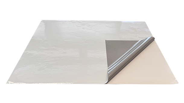 Es wird ein großes, dünnes, rechteckiges Blatt mit glänzender, metallischer Oberfläche gezeigt, bei dem eine Ecke teilweise abgelöst ist und so eine darunterliegende, andere Textur sichtbar wird.