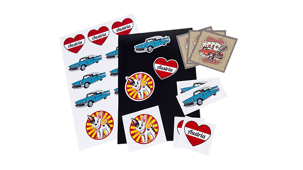 Eine Kollektion farbenfroher Aufkleber mit blauen Oldtimern, Herzmotiven mit dem Schriftzug „Österreich“ und runden Motiven mit einem Comic-Hund. Außerdem gibt es zwei bedruckte Karten im Vintage-Stil mit Illustrationen klassischer Autos.