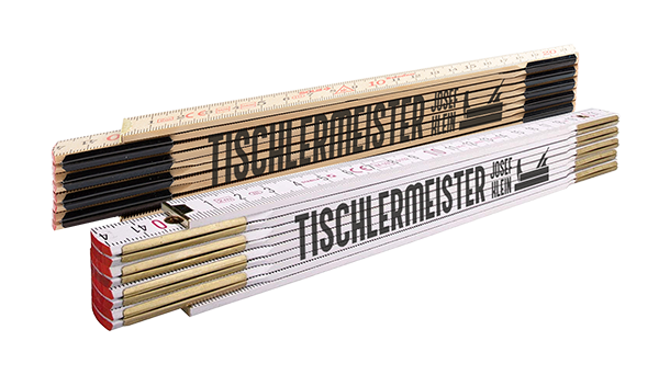 Zwei Klapplineale, eines aus Naturholz und eines aus weißem Holz, liegen übereinander. Beide Lineale sind mit einem Logo und dem Schriftzug „TISCHLERMEISTER JOSEF HELM“ in fetten schwarzen Buchstaben bedruckt.