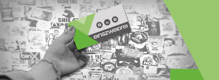 Eine Hand hält einen rechteckigen Aufkleber mit grün-weißem Design und Aufdruck