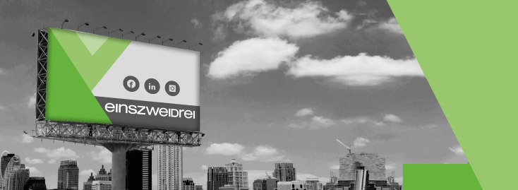 Große Werbetafel im Außenbereich vor der Skyline einer Stadt, mit einem grünen geometrischen Design, Symbolen für Facebook, LinkedIn und Instagram sowie dem Wort „einszweidrei“ auf überwiegend schwarz-weißem Hintergrund mit grünen Akzenten.
