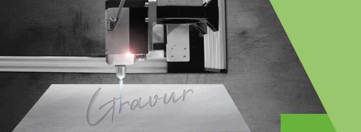 Eine Lasergravurmaschine verwendet einen fokussierten Laserstrahl, um das Wort „Gravur“ in eine flache, helle Oberfläche einzugravieren, wobei ein Teil des Hintergrunds durch ein grünes Dreiecksmuster hervorgehoben wird.