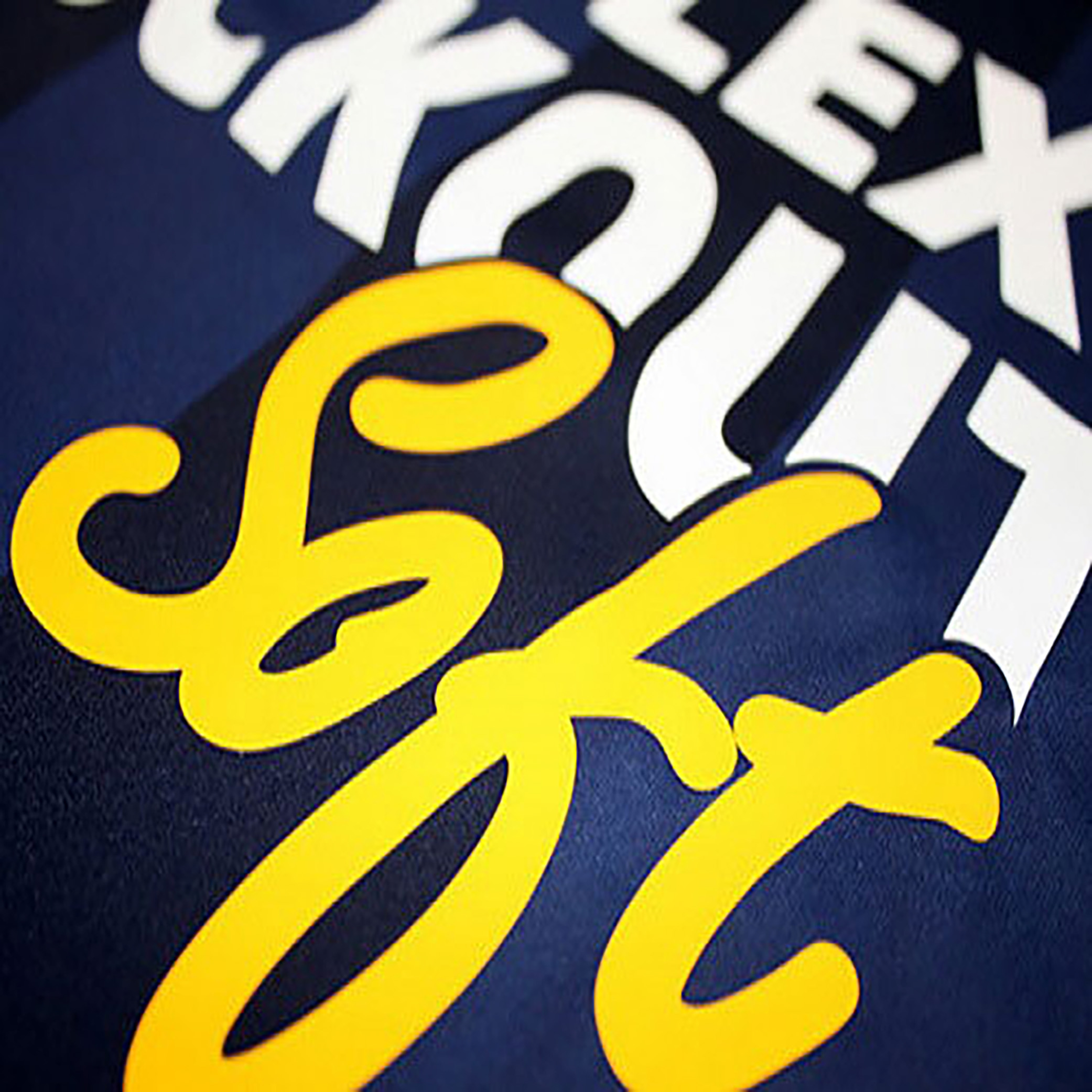 Close-up of overlapping stylized text on a dark background, with bold yellow script over white block letters. The text is partially cropped and difficult to fully read.